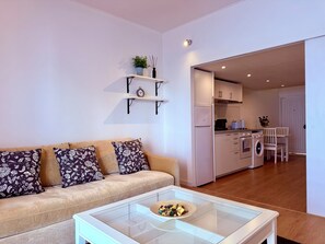 Ein modernes Wohnzimmer mit einer Couch, einem Glastisch und einer Küche im Hintergrund.
