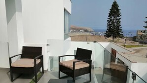A balcony with two wicker chairs and a glass railing overlooking a coastal area. - De-stress in the tranquility of the beautiful bay (Pucusana)