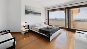 Une chambre à coucher moderne, avec un lit, des tables de chevet, une commode, une grande fenêtre et une vue sur le paysage.