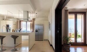 Une cuisine moderne dotée d’un îlot central, d’appareils électroménagers en acier inoxydable et donnant sur un balcon extérieur.