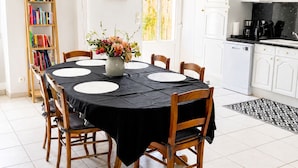 Un coin repas avec une table ronde, des chaises, une bibliothèque et, au fond, une cuisine.