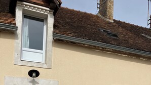 Un bâtiment à la façade beige, une porte blanche avec un panneau de verre, une petite fenêtre et une table avec des chaises à l’extérieur.