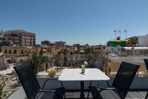 Terrassa al terrat amb taula i cadires, amb vista a una zona urbana densa i amb diversos edificis sota un cel serè.