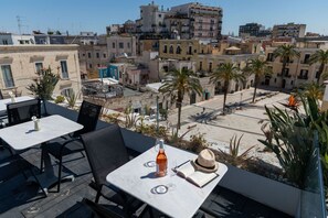 Zona d'estar a l'aire lliure amb taules i cadires, una ampolla de vi i un llibre.