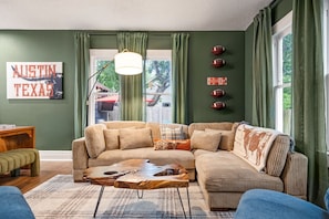 Ein gemütliches Wohnzimmer mit einem Ecksofa, einem Couchtisch und einem Fenster mit Vorhängen.