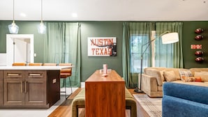 A modern living room with a wooden dining table, a blue sofa, and a kitchen area with a countertop and cabinets.