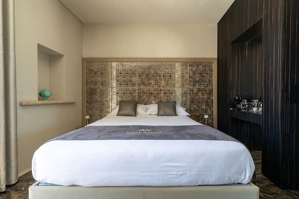 Ein Hotelzimmer mit einem großen Bett, einem dekorativen Kopfteil, einer kleinen Ablagefläche und einer dunklen Holztür.