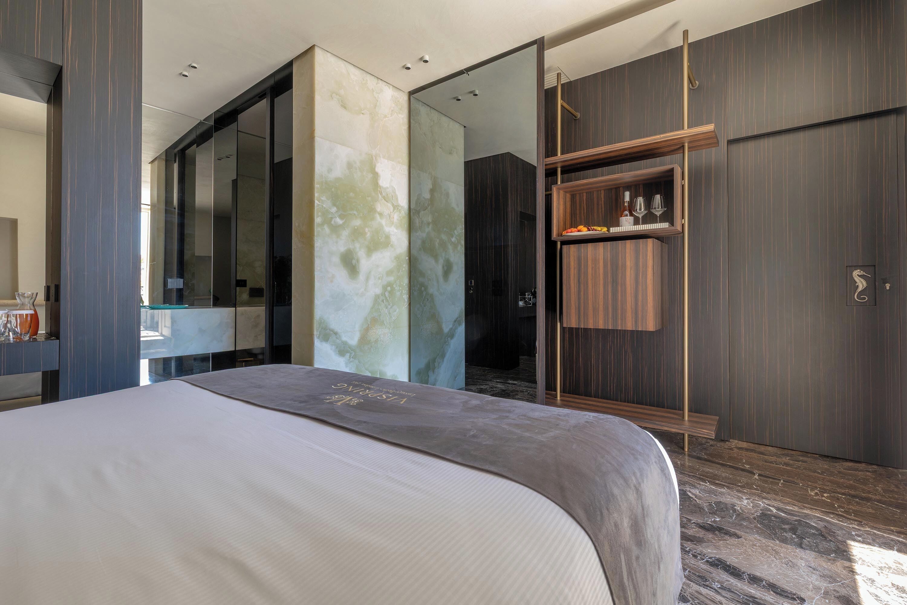 A modern hotel room with a large bed, a wardrobe, and a bathroom visible through a glass partition.