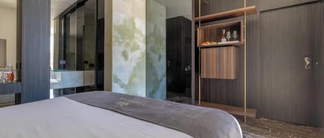 A modern hotel room with a large bed, a wardrobe, and a bathroom visible through a glass partition.