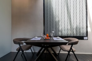A dining area with a dark wooden table, two brown chairs, a patterned wall, and a window with blinds. - Harbour - Junior Suite Sea Breez (Trani)