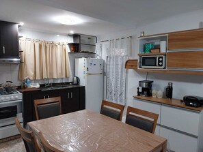 A compact kitchen with a stove, microwave, and refrigerator, a dining table with chairs, and a window with curtains. - mar de cobo refugio entre el lago y el mar (Parque Lago)