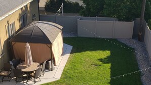 Ein Garten mit Rasen, einer überdachten Terrasse und Blick auf eine ferne Landschaft.