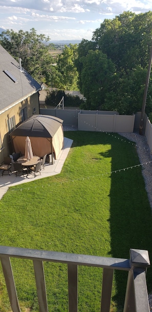 A backyard with a lawn, a covered patio area, and a view of a distant landscape.