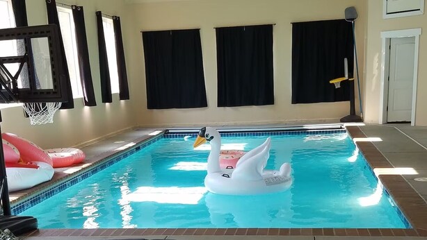 Ein Hallenbad mit einer Schwane als Schwimmspielzeug, schwarzen Vorhängen und einem Basketballkorb.