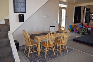 A dining area with a wooden table and chairs, a framed inspirational quote on the wall, and a basketball hoop in the background.