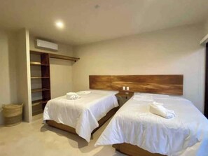 Habitación de hotel con dos camas, cabecera de madera, estante empotrado y un pequeño cubo de basura.