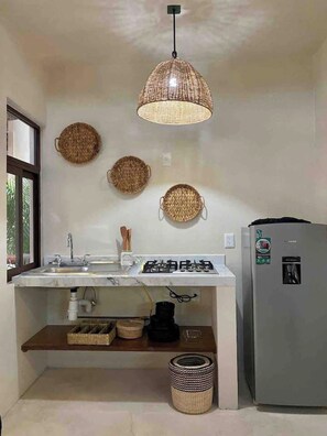 Una cocina con estufa a gas, un lavamanos, un refrigerador y cestas tejidas en la pared.