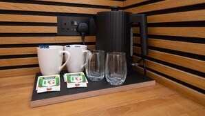 A kitchenette with a coffee maker, two mugs, two glasses, and two packets of tea. - Amber Serviced Accommodation Rooms (Hull)