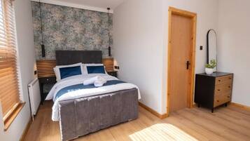A bedroom with a bed, bedside tables, a dresser, a door, and a wall with a textured pattern.