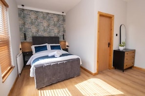A bedroom with a bed, bedside tables, a dresser, a door, and a wall with a textured pattern.