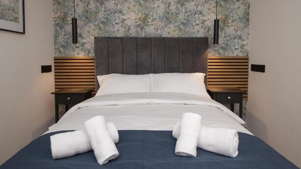 A neatly made bed with white linens and towels, a dark headboard, and a textured floral wallpaper. - Amber Serviced Accommodation Rooms (Hull)