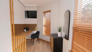 A modern room with a wooden desk, a black chair, a black dresser, a mirror, and a TV mounted on the wall. - Amber Serviced Accommodation Rooms (Hull)