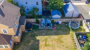 En boligs baghave med trampolin, overdækket terrasse og et indhegnet legeområde.
