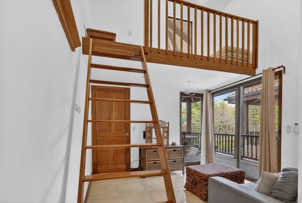 Ein Loft-Zimmer mit einer Holzleiter zu einem Balkon, einer Couch und einem kleinen Tisch.