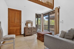 Ein geräumiges Wohnzimmer mit einer Couch, einer Holztür, einem kleinen Tisch und Blick ins Freie.
