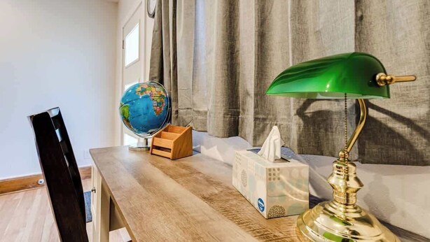 A wooden desk with a globe, a tissue box, and a green desk lamp.