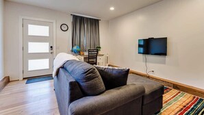 Ein Wohnzimmer mit einer Couch, einem Fernseher, einer Tür und einem Fenster mit Vorhängen.