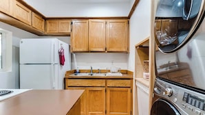 Eine kompakte Küche mit Holzausstattung, einem weißen Kühlschrank, einer Spüle und einer integrierten Waschmaschine.