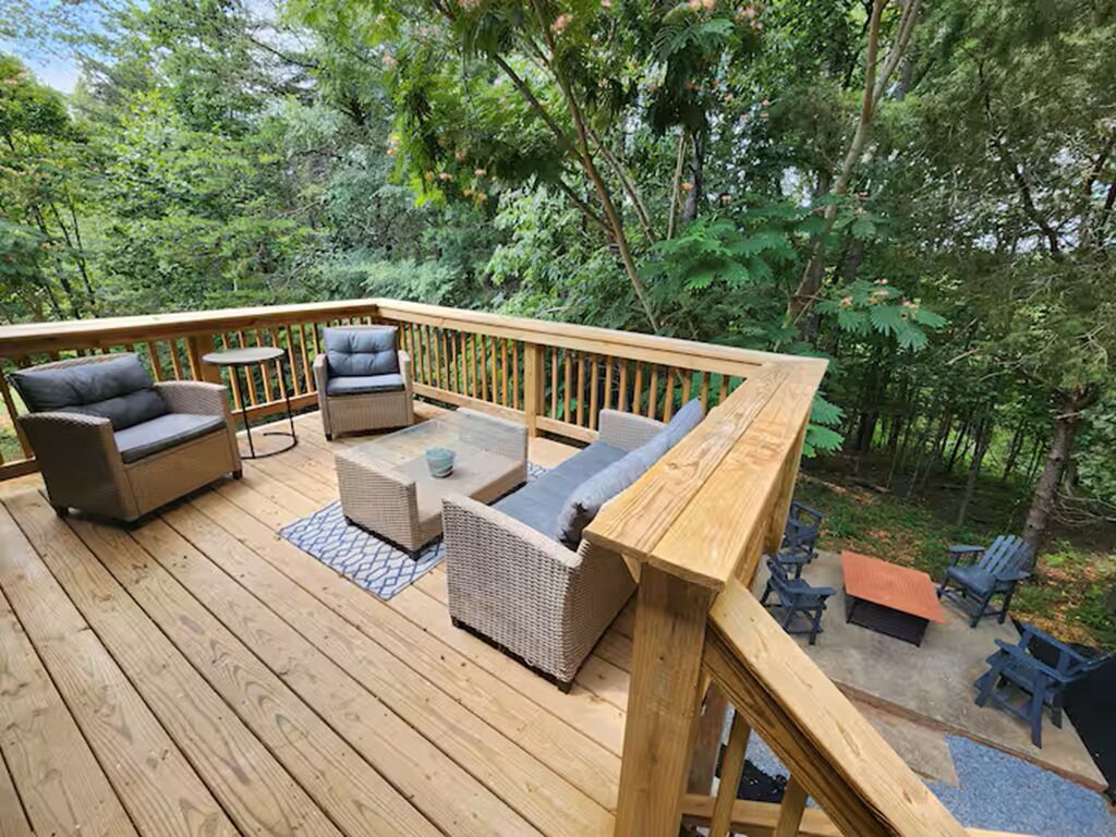 Een houten terras met tuinmeubilair, zoals banken en stoelen, omringd door bomen.