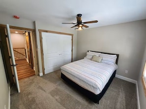 A bedroom with a bed, a ceiling fan, a door, and a staircase leading to another room.
