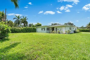 A single-story house with a front porch, surrounded by a well-maintained lawn and palm trees. - 2BR Getaway| Near Beaches, Aventura & Stadium (Miami)