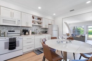 A modern kitchen with white cabinetry, a built-in oven, and a dining area with a round table and chairs. - 2BR Getaway| Near Beaches, Aventura & Stadium (Miami)