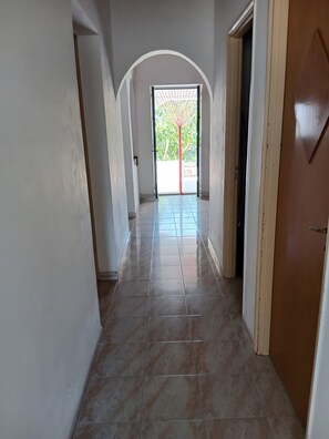 A hallway with a tiled floor, white walls, and a wooden door on the right. - Holiday Home 'Marzamemi Home' with Private Terrace, Garden and Air Conditioning (Noto)