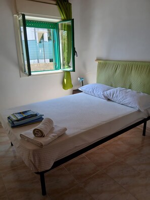 A single bed with a green headboard, a bedside lamp, and a window with green curtains. - Holiday Home 'Marzamemi Home' with Private Terrace, Garden and Air Conditioning (Noto)