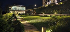 A modern building with a glass facade, a well-maintained lawn, and a wooden play structure. - Charming 2-bedroom apartment in Carretera a el Salvador near Casa de Dios. (Ciudad de Guatemala)