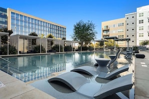 A swimming pool with lounge chairs, a pergola, and modern buildings in the background. - Cozy 1-bedroom apartment in charming Plano (Plano)