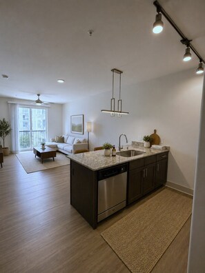 A modern kitchen with a central island, stainless steel appliances, and a dining area with a sofa and table. - Cozy 1-bedroom apartment in charming Plano (Plano)