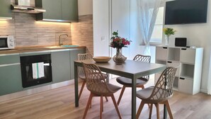 Eine moderne Küche mit Mikrowelle, Backofen und Spüle. Ein Esstisch mit Stühlen und eine Vase mit Blumen sind vorhanden. Ein Fernseher ist an der Wand befestigt.