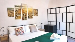 Ein Hotelzimmer mit Bett, Nachttisch, Lampe, einer Wand mit Kunstwerk und einer schwarzen Raumtrennung.