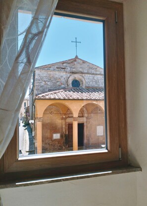 Blick aus dem Fenster auf ein Gebäude mit einem Kreuz auf dem Dach, Rundbögen und einem Ziegeldach.