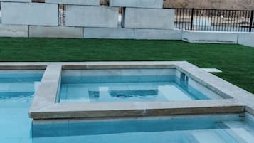 A rectangular swimming pool with a stone border, surrounded by a grassy area and a stone wall.