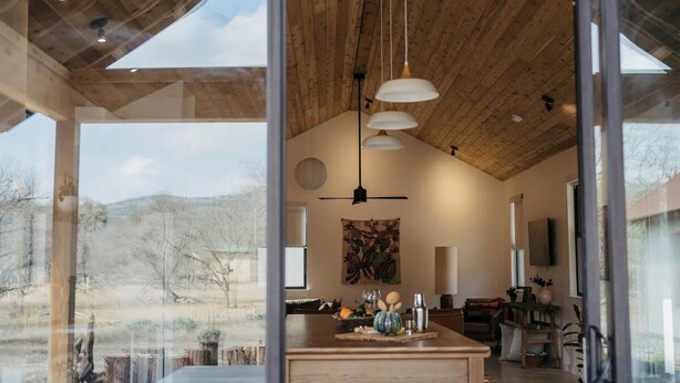 A modern interior with a wooden ceiling, a dining area with a table and chairs, and a view of the outdoors.