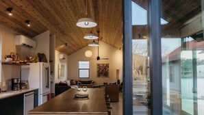 A modern kitchen with a central island, wooden ceiling, and large windows.