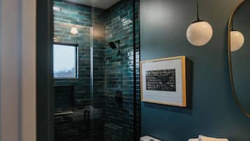 Un baño moderno con cabina de ducha de vidrio, inodoro, lavamanos y un cuadro en la pared.