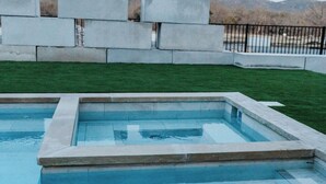 A rectangular swimming pool with a stone border, surrounded by a grassy area and a stone wall. - Secluded Ranch Stay up to 4 | Near Garner State Park and few steps to Frio River (Concan)