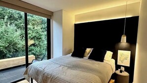 A modern bedroom with a large bed, a nightstand, a hanging light, and a view of greenery outside. - Secluded Ranch Stay up to 4 | Near Garner State Park and few steps to Frio River (Concan)